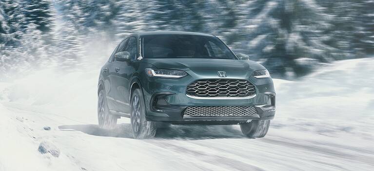 2027 Honda HR-V EX-L in Nordic Forest Pearl front driving through a snowy winter landscape (Subcompact Crossover SUV).